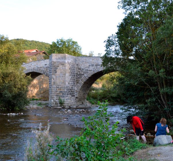 Peregrinos refrescan sus pies en el río Arga, ante el puente de Zubiri. Imagen de  José Holguera(www.grabadoyestampa.com) para guiarte.com.