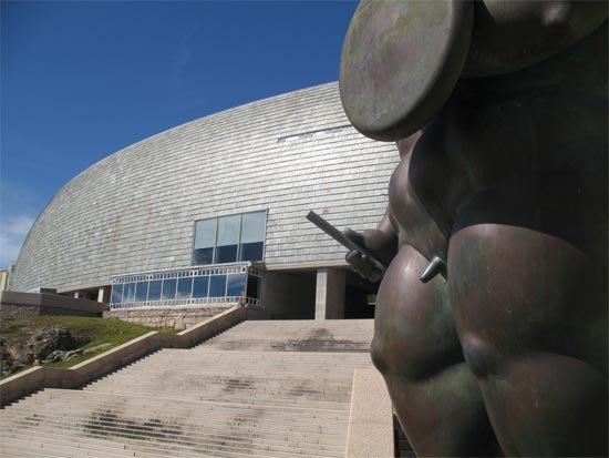 Fachada delantera de la Domus, en La Coruña, con la estatua de Botero, en primer término. Imagen de guiarte.com.