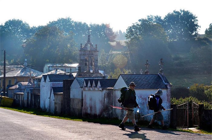Peregrinos avanzan ante el cementerio e iglesia de Ferreiros Lugo. Imagen de Jose Holguera para Guiarte.com