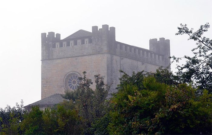La iglesia iglesia-fortaleza de San Juan, emergiendo entre el verdor y la niebla. Una imagen evocadora de Puertomarín. Imagen de José Holguera para Guiarte.com