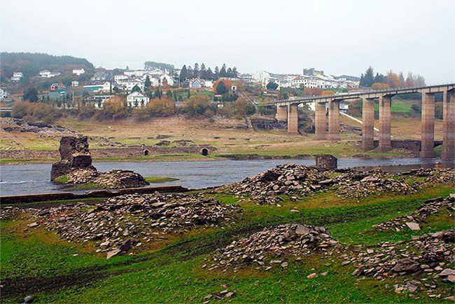 Puertomarín, desde el fondo del valle, con ruinas del viejo asentamiento, en primer plano y el nuevo puente. Imagen de www.concellodeportomarin