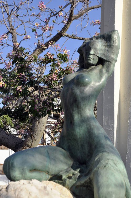 Monumento de Denia a la climatología benigna de la ciudad, representada por una joven mujer, en medio de una vegetación tropical. Guiarte.com