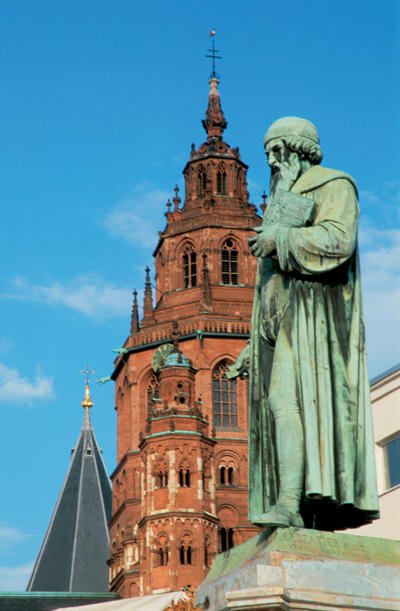 El monumento a la memoria de Gutemberg, en el centro de la ciudad, se recorta sobre el cimborio de la catedral. Imagen de Scherf, Dietmar. Turismo Alemán.
