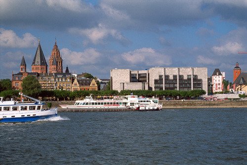 Imagen de la ciudad, desde el Rin, con las torres de la catedral, la sede municipal, y el campanario rojizo de la iglesia de San Quintín. Imagen de Kiedrowski, Rainer. Turismo Alemán.